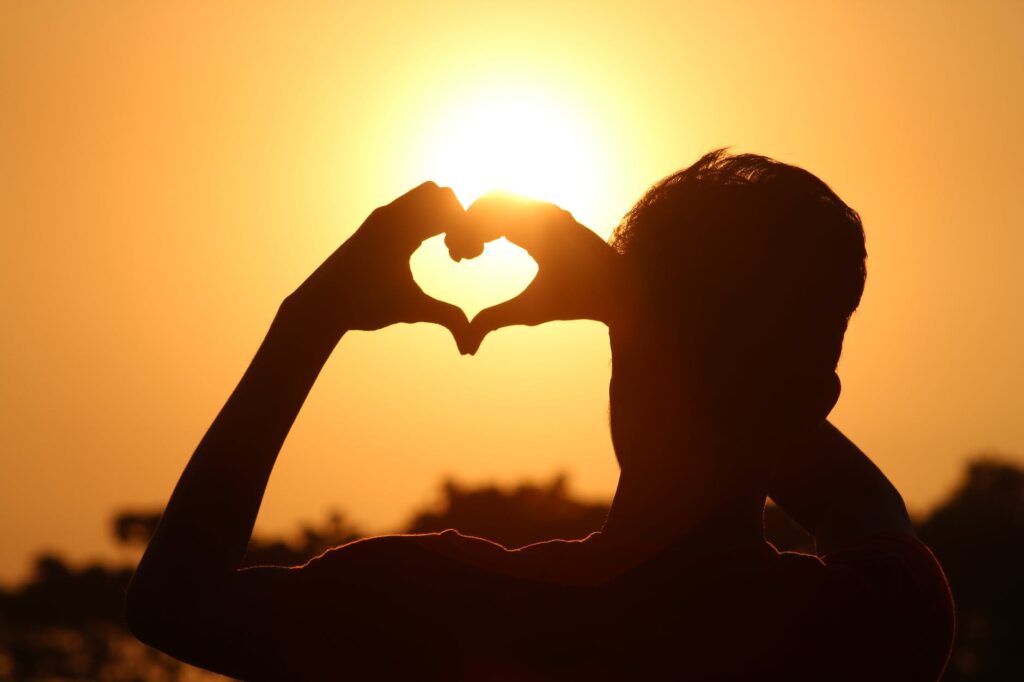 silhouette photo of man doing heart sign during golden hour